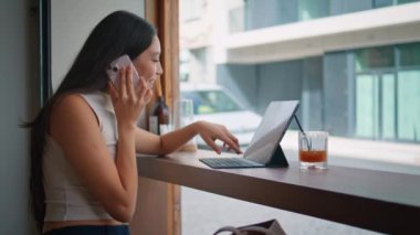 Çinli bir kız şehirdeki kahvecide laptoptan alışveriş için arama yapıyor. Kafeterya vitrininde konuşan gülümseyen esmer kadın. Uzaktan kumandalı mutlu işçi dostça konuş..