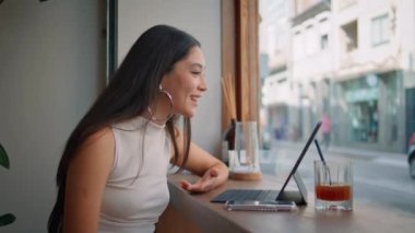 Asyalı kadın videosu çağdaş kafede dizüstü bilgisayar arıyor. Gülümseyen çekici kız modern barda oturmuş bilgisayar kamerasıyla konuşuyor. Mutlu stil sahibi iş kadını uzaktan kumandayla güler.