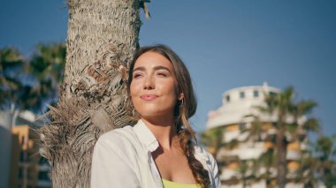 Arka sokakta ısınan gevşek güneş ışınları. Güneşli doğada gülümseyen mutlu gezgin kız tropikal ağaç ortamında dinleniyor. Neşeli kadın tatilin tadını tek başına çıkarıyor. Hafta sonu etkinlik kavramı