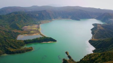 Sabah havadaki volkanik ada gölü. Dalgalanan turkuaz su, yazın kayalık kıyı şeridini yıkıyor. İnsansız hava aracı deniz kenarındaki dağların üzerinde uçuyor. Panoramik pelerin manzarası. Çarpıcı doğa manzarası.