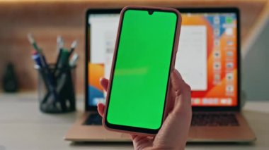 Kimliği belirsiz bir kız Chroma Key cep telefonuyla şirket ofisinde çalışıyor. İş yerinde elinde yeşil ekran cep telefonu tutan kadın elleri. Mockup smartphone 'da bayan yönetici tarama uygulaması.