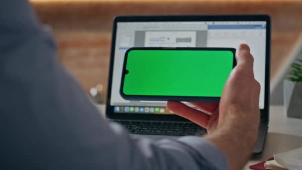 男子手指敲绿色屏幕智能手机在办公室工作台的特写 无法辨认的公司员工在笔记本电脑工作场所通过模拟手机阅读消息 男性手拿着色键电话 — 图库视频影像