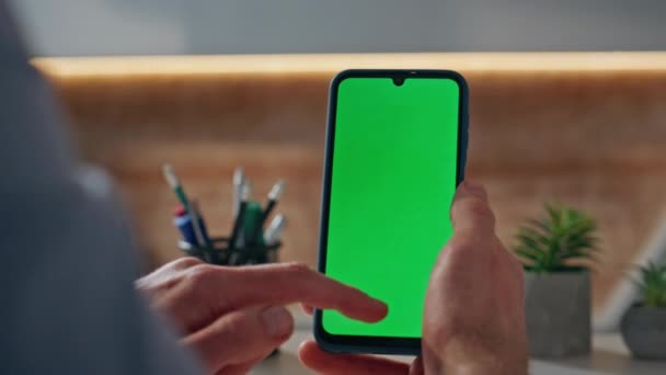 キャビネットのクローズアップでクロメイクスマートフォンをスクロールするビジネスマン テーブルにテンプレートデバイスを保持するオフィスマン手 温かい光の職場でウェブサーフィンをする緑色のスクリーン携帯電話を使用して認識されていない従業員 — ストック動画