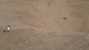 Sörfçü altın kumda yürüyor ve arkasında ayak izleri bırakıyor. Tanımlanamayan profesyonel sörfçü kumlu deniz kenarına elinde sörf tahtasıyla çıkıyor. Bilinmeyen aktif kişi yaz tatilinden zevk alıyor