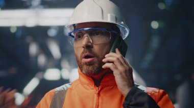 Fabrika teknik uzmanı telefon edip atölye ekipmanlarını kapatmaktan şikayetçi. Endişeli mühendisin endişeli akıllı telefon konuşması portresi. Üniformalı yapım işçisi cep telefonuyla kavga ediyor..