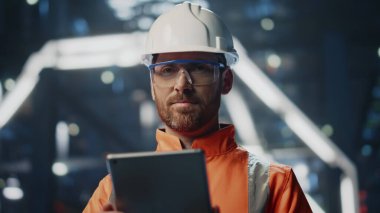 Tatmin olmuş fabrika müfettişi nalbur üretim tesisinde tablet üzerinde çalışıyor. Gülümseyen sakallı kalite kontrol kamerası. Üniformalı kalifiye teknisyen bilgisayardan not alıyor..
