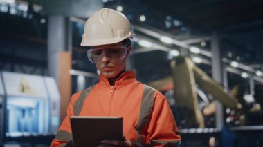 Denetleyici, fabrika ekipmanlarının kalitesini kontrol ediyor. Tablet kapanış çekimine not alıyor. Endüstriyel tesisi inceleyen ciddi kadın mühendis. Üniformalı yetenekli kadın teknisyen prodüksiyonda ped bilgisayar kullanıyor.