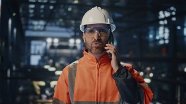 Metalurji üretiminde cep telefonundan konuşan neşeli bir fabrika tamircisi. Gülümseyen mühendis molada ayakta duran fabrikadan arıyor. Üniformalı mutlu sanayi işçisi akıllı telefondan konuşuyor..