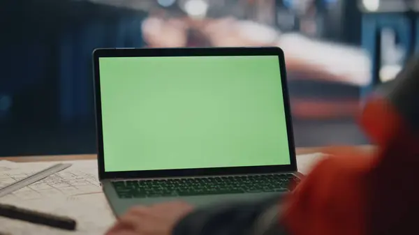 Green screen laptop on factory specialist table close up. Unrecognized engineer looking in mockup monitor analysing production data. Unknown architect working at computer creating technical project.