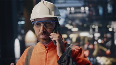 Mutlu fabrika işçisi endüstriyel tesisten arıyor. Başarıyı yakın planda hissediyorum. Korumalı miğfer takan duygusal profesyonel mühendis akıllı telefondan konuşuyor. Üretim elemanı üniformalı cep telefonuyla konuşuyor.