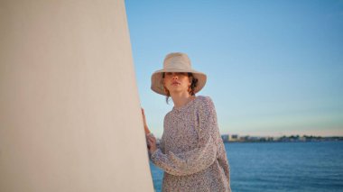 Hafta sonları günlük model dinlenme evi. Gölde poz veren şapkalı güzel sakin bir kadın. Kameraya bakan rahat genç gezgin yaz tatilinin tadını çıkarıyor. Huzurlu manzaralı gezgin kadın