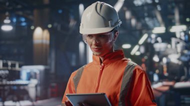 Endüstriyel uzmanlar imalat tesisini tabletle kontrol ediyorlar. Üretim sürecini kontrol eden kadın mühendis. Modern fabrikada çalışan kask giymiş kadın teknisyen.