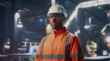 Fabrika atölyesinde el ele tutuşan profesyonel bitki uzmanı portresi. Koruyucu kask üniformalı yetenekli mühendis kameraya yakından bakıyor. Yapım üzerine sakallı tamirci pozu