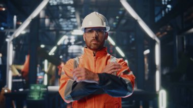 Gururlu imalatçı kamera görüntüsü, yakından gülümsüyor. Portre, modern üretim atölyesinde el ele tutuşan bir fabrika mühendisi niteliğinde. Sanayi bölgesinde poz veren sakallı fabrika işçisi.