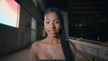 Dreadlocks esmer görünümlü kamera akşam sokak portresi. Gece şehir merkezinde yalnız poz veren mutlu muhteşem bayan. Şehirdeki yaratıcı fütüristik makyajlı Afrikalı Amerikalı model kadın.