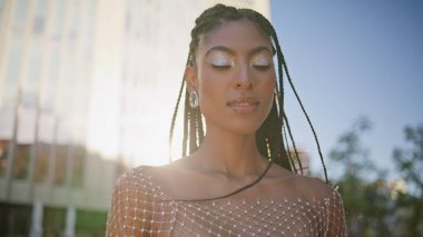 Rüzgarlı esmer, güneş ışığı kare resminde poz veriyor. Makyaj makinesi olan afro saçlı kadın yaz sokağı kapanışında kendini rahat hissediyor. Şehir merkezine bakan esmer tenli kadın.