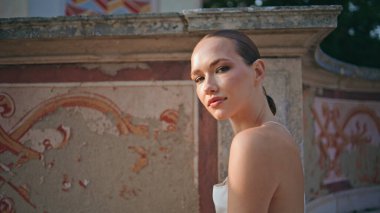 Antika duvar yerindeki muhteşem turist görünümlü kamera yakın plan. Tatil gezisinde yaz güneşinin tadını çıkaran çekici kadının portresi. Eski Victoria süslemelerinin önünde şehvetli bir poz..