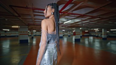 Dreadlocks 'un kamerasını çeviren kadın koyu uzay arka görüşünde saça dokunuyor. Afro saç stili, şık bir kız gece şehir otoparkında poz veriyor. Kahverengi tenli, rahat kadın yeraltında vakit geçiriyor.