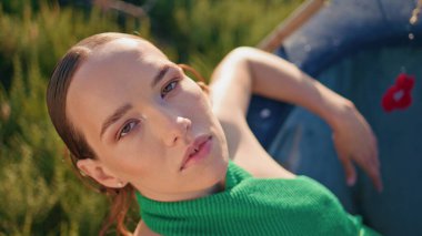 Akşam güneşinde poz veren açık hava kızı portresi. Yaz tatilinde yeşil tarlada dinlenen şık bir kadın. Kırsal çayırdaki kameraya bakan çekici romantik kadın yüzü. Şehvetli model çiftlik arazisinde rahatla