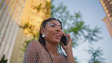 Akşam saatlerinde tek başına konuşan siyah saçlı bir model. Şık bir Afrikalı Amerikalı kadın güneşli bir mahallede cep telefonu sohbeti yapıyor. Çekici moda kızı akıllı telefondan arıyor.