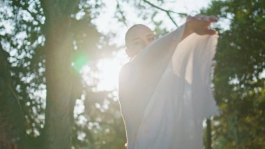 Parlak yaz güneşinin önünde beyaz bezle el sallayan romantik kız. Yeşil parkta duran güneş ışınlarında poz veren muhteşem genç bir kadın. Zarif güzel bayan yumuşak hareketler yapıyor, güneşin tadını çıkarıyor..