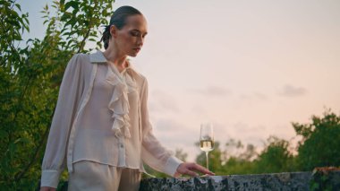 Çekici kız akşam gökyüzünün önündeki taş çitlerin balkonunda şarap kadehi görüyor. Sakin, güzel bir kadın terasta şampanyayla kadeh tokuşturuyor. Yalnız bayan hafta sonunun tadını çıkarıyor..