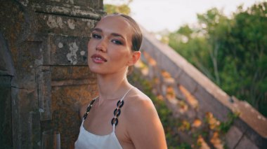 Güzel bayan, şarap kadehiyle eski binaya bakıyor. Ortaçağ şatosunda akşam vakti poz veren çekici gülümseyen kadın portresi. Antik sarayda duran zarif genç kız..
