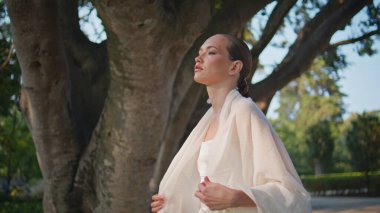 Nazik kız ağacın altında duruyor ve yakından bakıyor. Beyaz elbiseye sarılmış çekici, ciddi bir kadın akşam vakti parkta üşüyor. Hayalperest genç bayan sakin bir hafta sonunun tadını çıkarıyor..