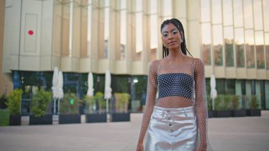 Koyu tenli model şehir meydanında tek başına fotoğraf makinesi pozu veriyor. Afro örgü ören kadın gösterişli kıyafetlerini sergileyerek boş merdivenlerden geçiyor. Havalı görünümlü kadın çantasıyla yaz havasının tadını çıkarıyor. Halk yaşam tarzı konsepti