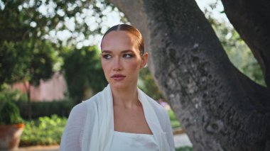 Zarif kız parka gidiyor. Kameraya yakından bakıyor. Ciddi, rahat bir kadın yeşil bahçede yürüyor ve güzel bir bahar haftasonunun tadını çıkarıyor. Beyaz elbiseli güzel bayan güneşli doğada geziniyor..