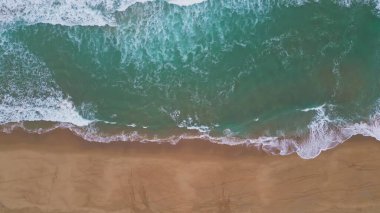 Turkuaz okyanus suyu kumlu sahil manzarasını yıkıyor. Güzel, sakin deniz dalgaları boş deniz dronu çekimine geliyor. Süper yavaş çekimde tropikal sahil şeridinde fokurdayan resimli sörf. Kıyı güzelliği.