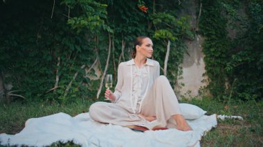 Rahat kadın güzel yeşil cam çayırlarda pikniğin tadını çıkarıyor. Kaygısız çekici kız cam kadehte beyaz şarap tutuyor battaniyenin başında oturuyor. Güzel bayan gözlerini kapatıyor. Doğa ile ilgili kitapla rahatlıyor..