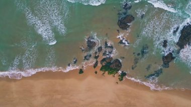Sakin dalgalar kumlu sahil manzarasına akıyor. Turkuaz okyanus suyu güzel deniz kıyılarını kayalık taşlarla yıkıyor. Havadan çekilen mavi deniz sörfü süper yavaş çekimde yaz sahillerinde köpürüyor..