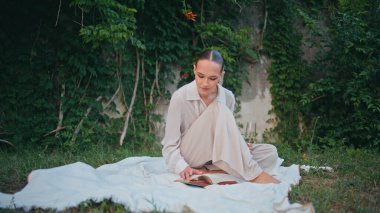 Serene Lady, Meadow 'da kaygısız piknikte sayfa çeviriyor. Rahat çekici kadın yeşil çimlerin üzerinde oturmuş ilginç bir roman okuyor. Muhteşem sakin kız haftasonu doğa hobisinin tadını çıkarıyor..