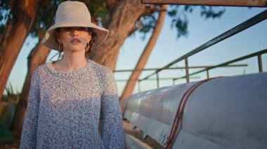 Nehir kenarındaki teknelerde kamp yapan güzel bir kadın. Akşam güneşinde poz veren şapkalı gezgin kız dışarıda dinleniyor. Günlük barışçıl model. Kameraya bak. Yaz tatilinin tadını çıkar.