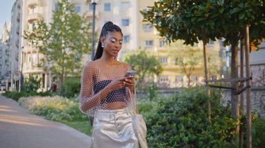 Summer Caddesi 'nin kapanışında akıllı telefonlara bakan mutlu bayan. Neşeli Afro-Amerikalı kadın şehir merkezindeki cep telefonuna mesaj atıyor. Moda kıyafetleri içinde cep telefonu cihazı tutan neşeli kız.