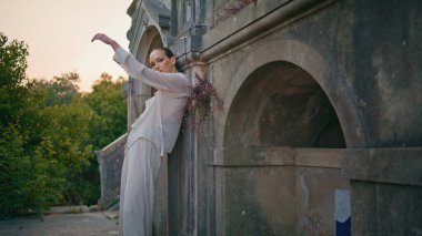 Eski duvarlara yaslanmış antik binada poz veren muhteşem bir model. Ortaçağ şatosuna bakan kendine güvenen güzel bir kadın. Terk edilmiş beyaz takım elbiseli şık bir model dışarıda duruyor..