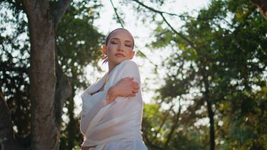 Rahatlamış bir kadın yaz güneşi altında kendine sarılıyor. Beyaz giysili çekici, hayalperest kız yeşil park güneşinin tadını çıkarıyor. Nazik genç bayan gözlerini kapatıyor. Güzel bahçe tek başına duruyor..