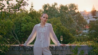 Balkonda poz veren kendine güvenen yaşlı kadın kameraya bakıyor. Taş çitlere dayanan şarap kadehiyle muhteşem zarif bir kız antik kalede. Güzel bayan, rüzgarda sallanan yeşil ağaçlarda duruyor..