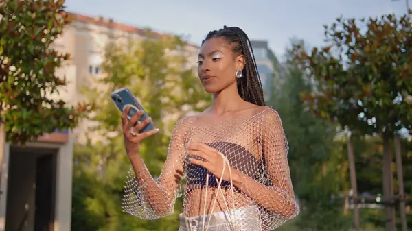 Afrikalı bir kadın şehirde selfie çekiyor. Şehir Yeşillik Parkı 'nda cep telefonu kamerası pozu veren muhteşem siyah saçlı kız. Havalı esmer kadın gülümsüyor. Yaz caddesinde tek başına fotoğraf çekiyor. 