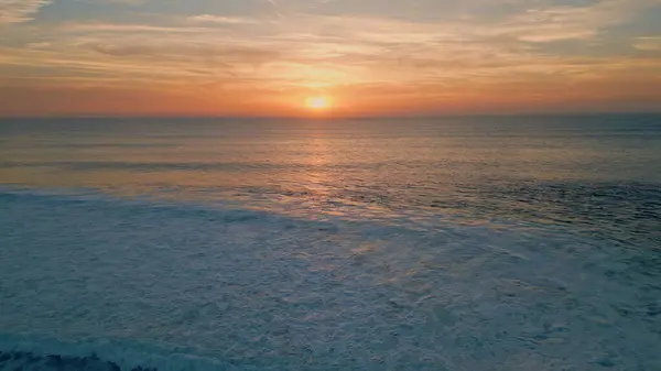 Bright sunset shining over sea surface drone view. Stunning summer sun setting down at endless ocean horizon. Beautiful waves foaming rippling under golden sundown light in slow motion. Marine beauty