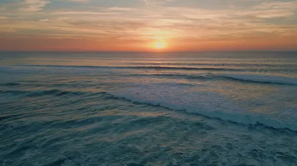 Golden sunset sky over ocean horizon aerial view. Picturesque summer sundown reflecting in foamy sea waves rolling to seashore in super slow motion. Orange sun setting down at tranquil marine evening.