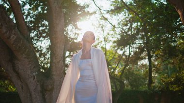 Siluet kadın, hava gibi beyaz giysiler içinde güneş ışığında poz veriyor. Yeşil güneşli parkta duran muhteşem zarif model. Gevşemiş çekici kız güzel bahçede yaz doğasının tadını çıkarıyor. Kadın güzellik konsepti.