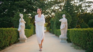 Sokakta antik mermer heykellerle dolaşan muhteşem bir kız. Güzel yeşil bahçede yürüyen zarif, güler yüzlü bir kadın. Kaygısız kadın akşamları beyaz örtüye sarılı parkta geziniyor..