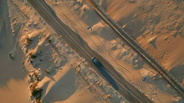 stock image Drone view desert highway running along sandy terrain summer day. Fast transport riding road between dunes in slow motion. Amazing golden sundown reflecting in sand surface. Vacation tourism concept