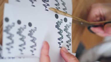 Kadın parmakları makas kağıdını dikey olarak kesiyor. Meçhul dövme sanatçısı masada çizimler yapıyor. Yaratıcı kadın elleri içeride ahşap masada ekipman kullanıyor. Anonim yaratıcı sanat stüdyosu