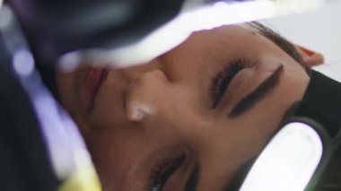 Mutlu sanatçı, kuaför salonundaki dikey portrede dövme kalemi kullanıyor. Siyah steril eldiven dövmecisi ev stüdyosunda çalışıyor. Gülümseyen kadın bilinmeyen bir müşterinin vücuduna el feneri takarak resim aktarıyor.