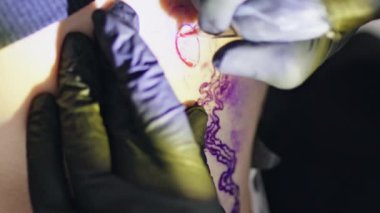 Usta eller kuaförde dikey olarak dövme yapıyor. Stüdyoda çalışan bilinmeyen dövme makinesi. Sanatçı parmakları, siyah eldiven giyen müşterinin vücudunda resim oluşturur. Yaratıcı işgal kavramı