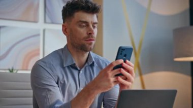 Ciddi bir işadamı cep telefonuna bakıyor modern ofis içlerini kapatıyor. Sakin sakin adam yönetici elinde akıllı telefonla dizüstü bilgisayarın iş yerinde keyfine bakıyor. Mesajlaşan yakışıklı adam.