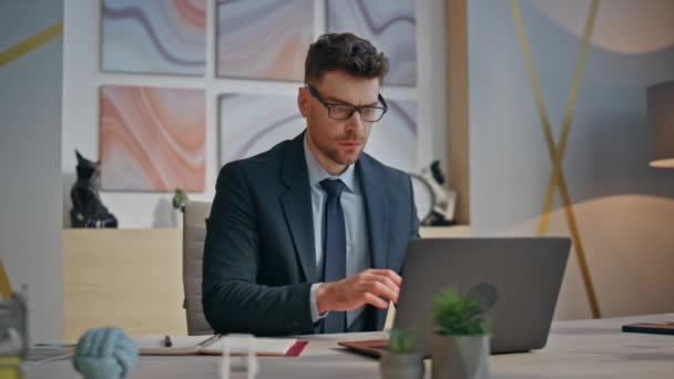 信頼できるビジネスマンは 現代的なインテリアのクローズアップでノートパソコンを動かします プロジェクトに関わるお茶を飲む眼鏡のスタイリッシュなマネージャー エージェンシーオフィスで真剣な上司がスクリーンを見ている ビジネスライフスタイル — ストック動画